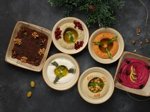 Bowls of hummus, muhammara and beetroot dip on a dark table